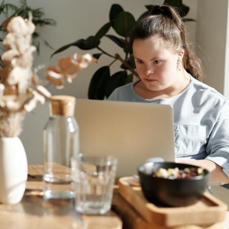 Eine junge Frau mit Down-Syndrom sitzt an einem Laptop