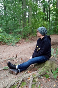 Eine Frau mit Mütze, die im Wald auf einem Baumstamm sitzt und die Natur beobachtet